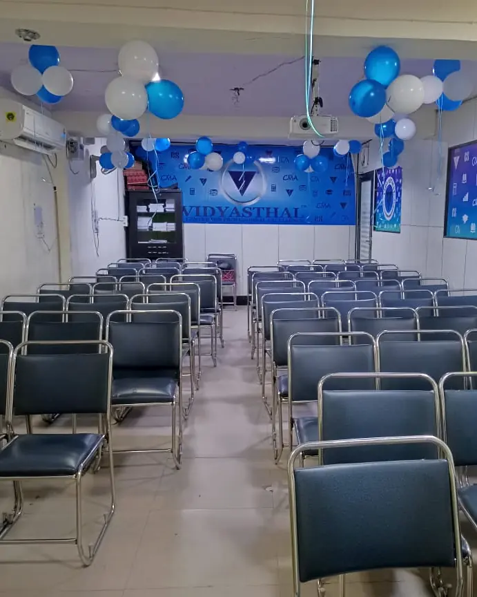 The classroom at Vidyasthal: rows of steel-framed chairs facing a blue board and a ceiling projector